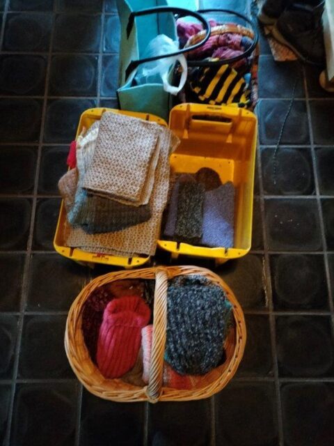 Strickwaren in Körben, Kisten und Taschen warten darauf, in die Kirche zum verteilen gebracht zu werden.