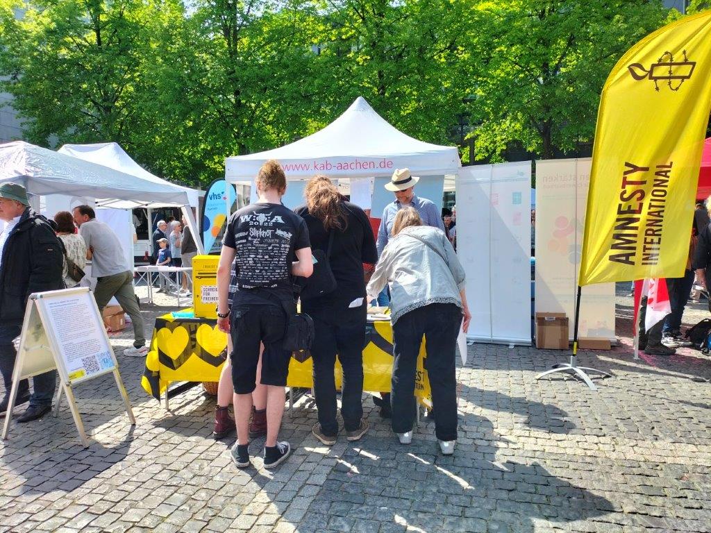 Menschen informieren sich am Amnesty-Infostand am 1.5.24 auf dem Aachener Katschhof