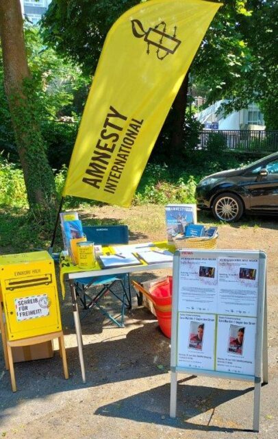 Amnesty Infostand auf dem Aachener Weltfest im Hintergrund eine Beachflag