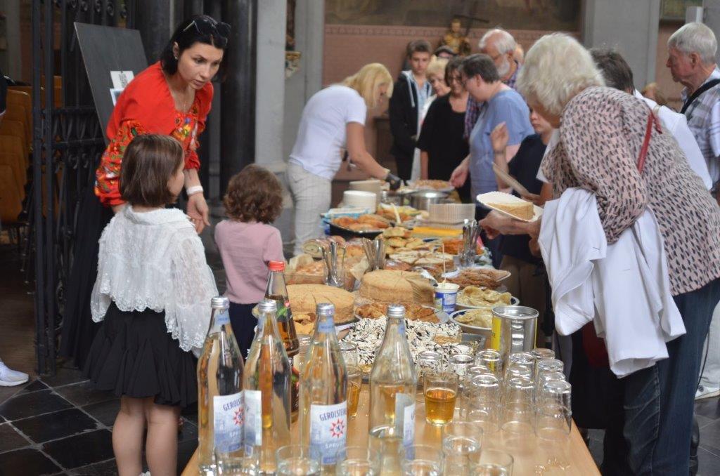 Menschen von klein bis groß bedienen sich am umfangreiche Buffet auf einem langen Tisch.