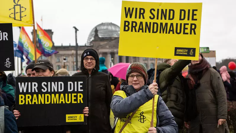 Demo vor dem Bundestag, Menschen halten Amnestyschilder mit der Aufschrift "Wir sind die Brandmauer" hoch.