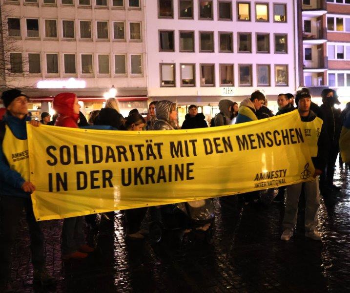 Menschen bei einer Mahnwache in Aachen zeigen ein Amnesty-Banner mit Aufschrift "Solidarität mit den Menschen in der Ukraine"