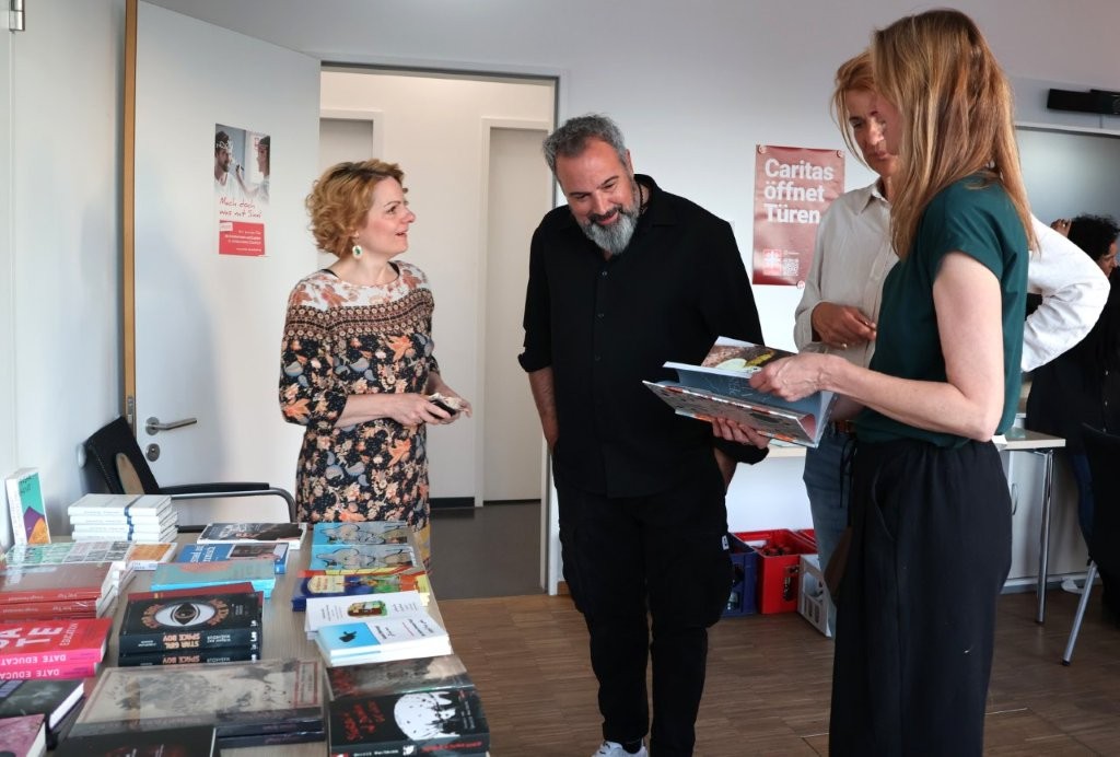 Vier Personen unterhalten sich am Büchertisch, z.T. mit aufgeschlagenen Büchern in der Hand.
