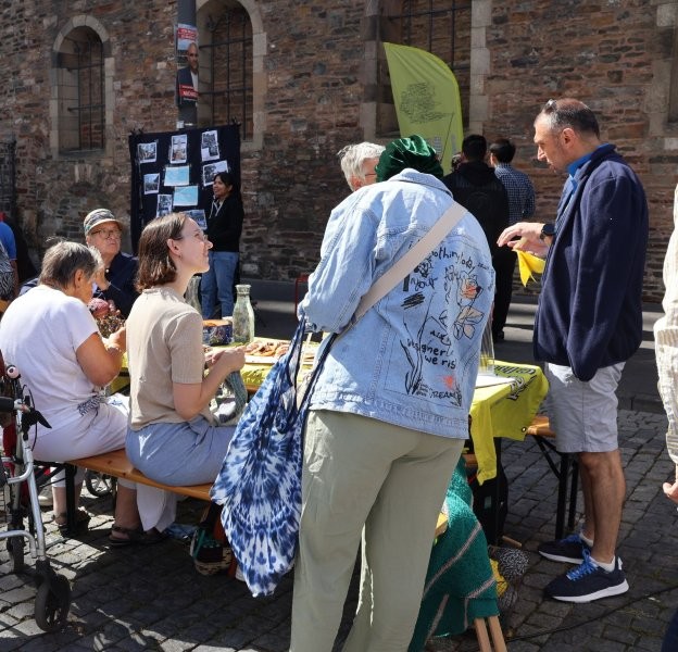 Strickende Menschen an einer Bierzeltgarnitur auf dem Aachener Katschhof. Andere Personen schauen sich bereits fertig gestrickte Stücke an.