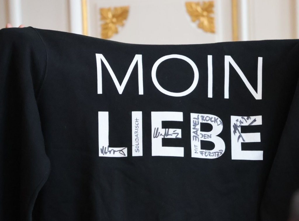 Schwarzes Sweatshirt mit weißer Aufschrift "Moin Liebe". In den großen weißen Buchstaben wurden Unterschriften angebracht.