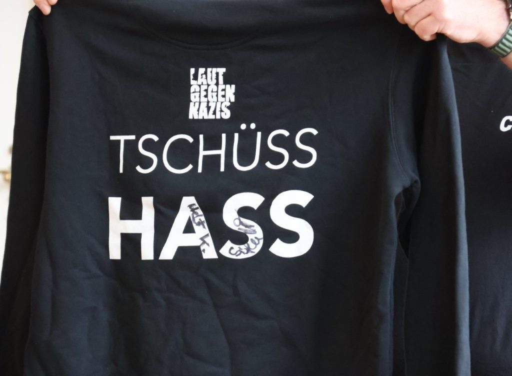 Schwarzes Sweatshirt mit kleiner Aufschrift "Laut gegen Nazis" und großer Aufschrift "Tschüss Hass".