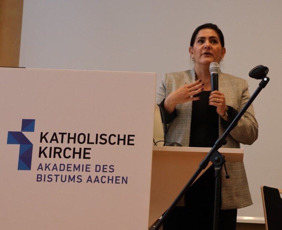 Eine Frau spricht an einem Pult der Akadamie des Bistums Aachen in ein Mikrofon.