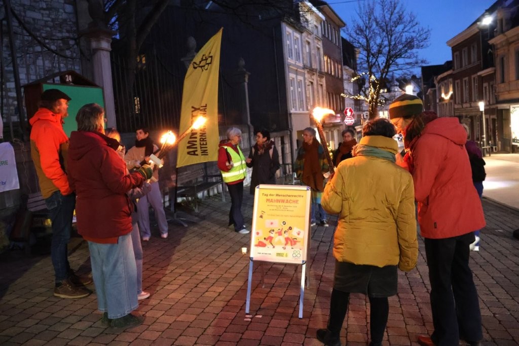 Menschen stehen mit Fackeln zur Mahnwache vor dem Tag der Menschenrechte an der Nikolauskirche in Eupen.
