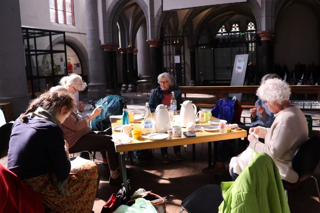 Mehrere Frauen sitzen mit Getränken und Tellern an einem Tisch und strickten in der Aachener Citykirche.