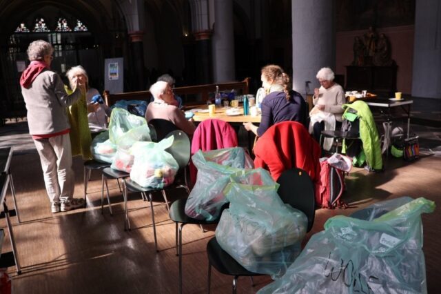 In mehreren Säcken liegt gesammelte Wolle in der Citykirche in Aachen. Im Hintergrund sitzen mehrere strickende Personen.