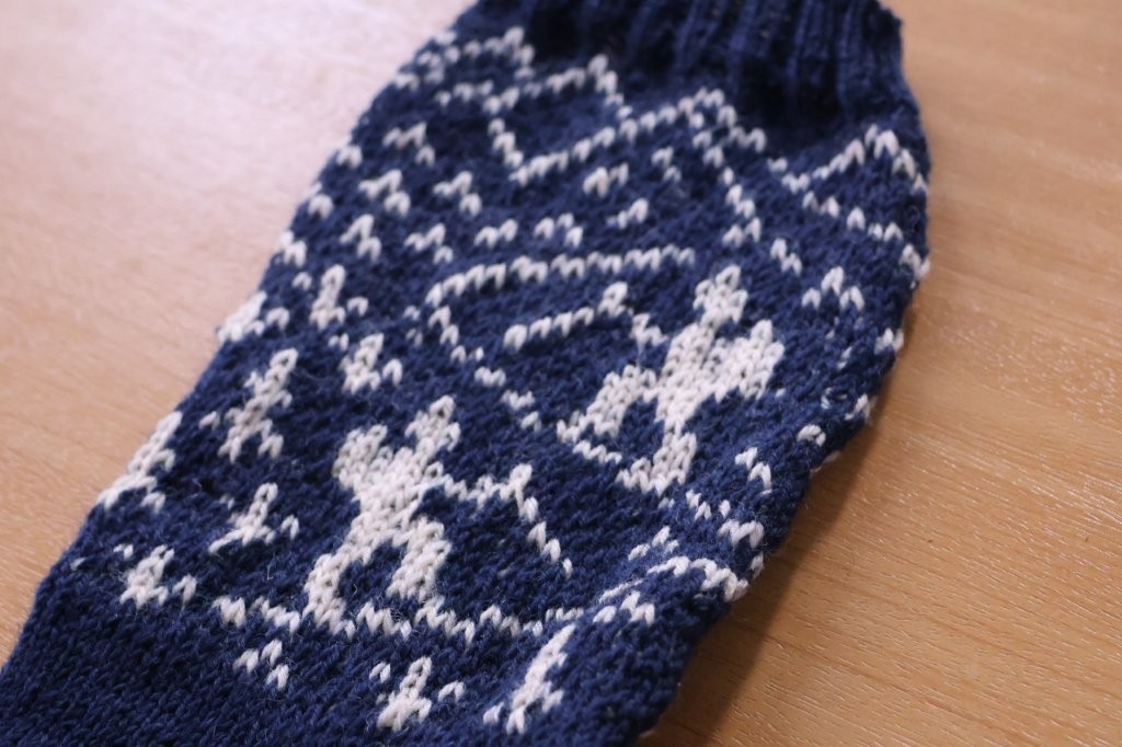 Eine dunkelblaue Stricksocke mit weißem Muster liegt auf einem Holztisch.