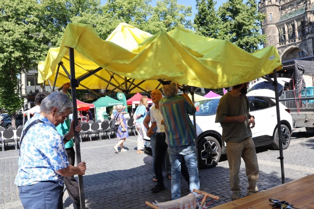Auf dem Aachener Katschhof werden Infostände aufgebaut. Ein gelber Pavillon wird gerade von mehreren Personen auseinandergezogen.